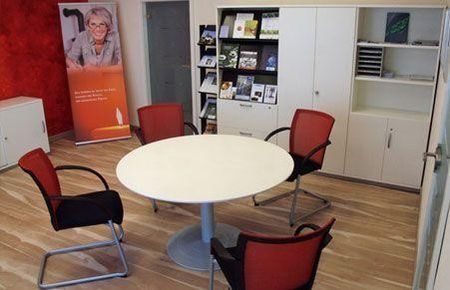 Büroraum mit einem runden Tisch, umgeben von roten und schwarzen Stühlen